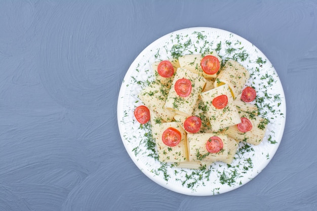 체리 토마토와 하얀 접시에 다진 허브와 펜 네 파스타.