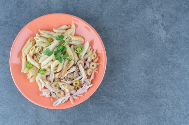 Penne pasta with chicken on orange plate. 