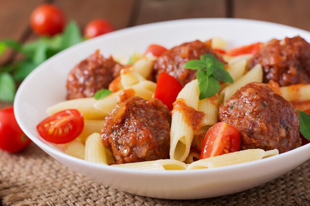 Penne pasta with meatballs in tomato sauce in a white bowl