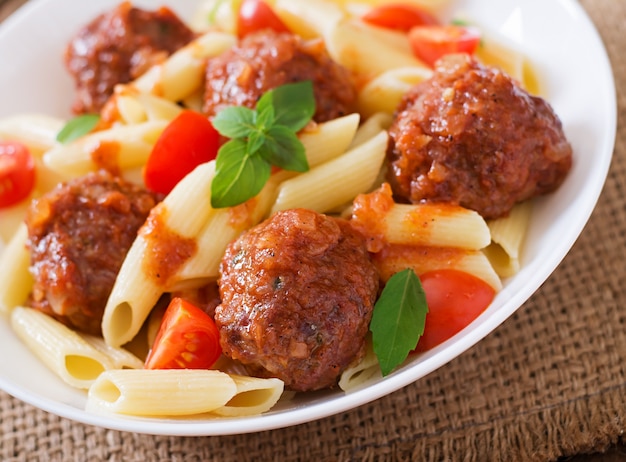 Penne pasta with meatballs in tomato sauce in a white bowl