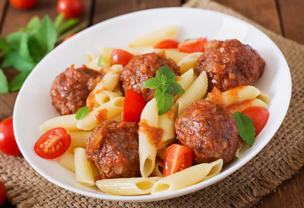 Penne pasta with meatballs in tomato sauce in a white bowl