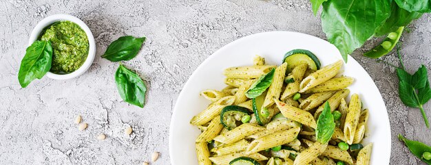 Penne pasta with  pesto sauce, zucchini, green peas and basil. Italian food. Top view. Flat lay