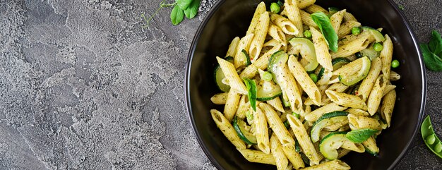 Penne pasta with  pesto sauce, zucchini, green peas and basil. Italian food. Top view. Flat lay