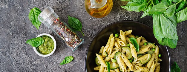 Penne pasta with  pesto sauce, zucchini, green peas and basil. Italian food. Top view. Flat lay