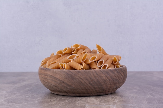 Penne pastas in a rustic wooden bowl on grey surface