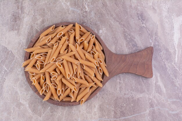 Penne pastas on a wooden platter on the marble