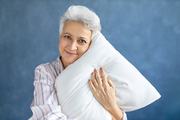 白い柔らかい枕をポーズして抱き締める年金受給者