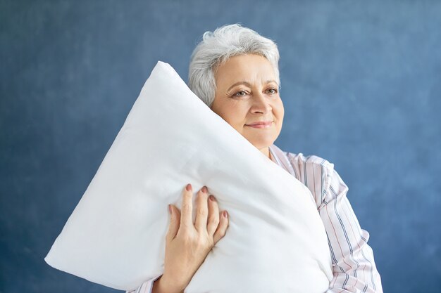 Pensioner posing and hugging white soft pillow