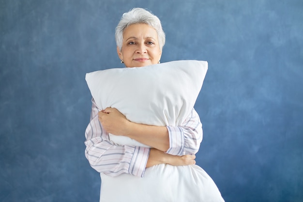 Pensioner posing and hugging white soft pillow