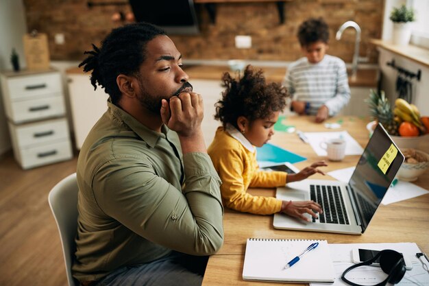 Pensive African American working father with his children at home