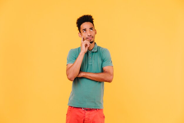 Pensive african guy with short hair looking up. Indoor photo of calm black male model in green t-shirt.