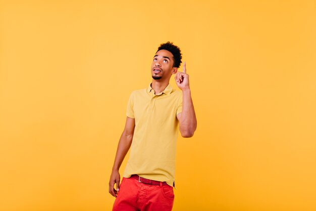 Pensive african model has an idea. Indoor shot of serious black man posing with finger up.