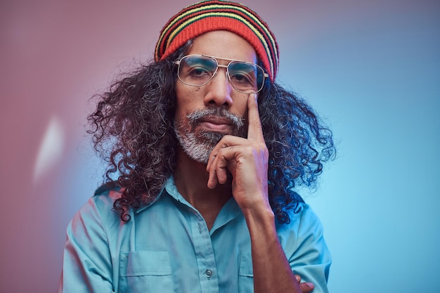 Free photo pensive african rastafarian male wearing a blue shirt and beanie. studio portrait on a blue background.