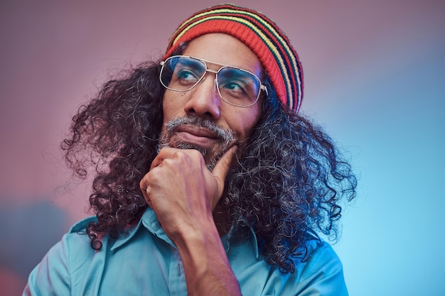 Pensive African Rastafarian male wearing a blue shirt and beanie. Studio portrait on a blue background.