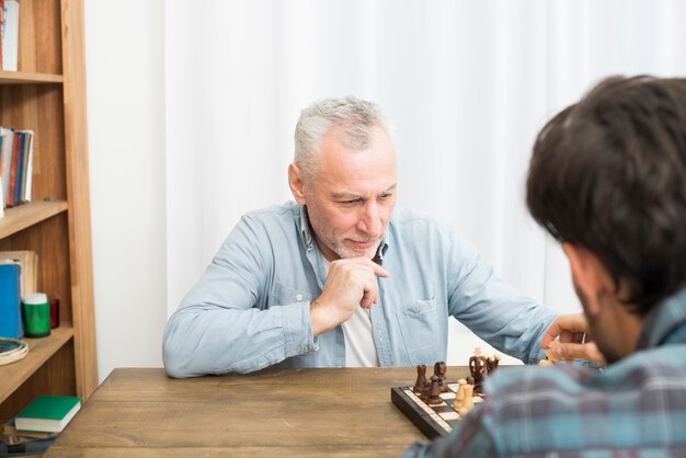 物思いにふける老人男性とテーブルでチェスをする若い男