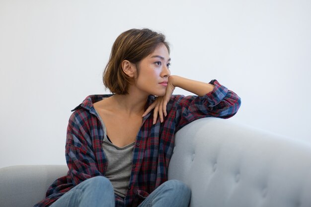 Pensive Asian girl on couch thinking over problems