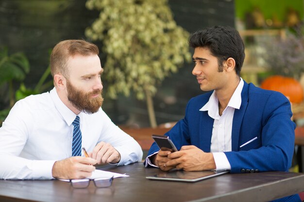Задумчивый бородатый мужчина разговаривает с деловым партнером в современном кафе