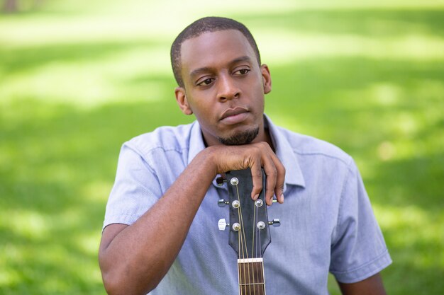 Pensive black man leaning on guitar headstock in park