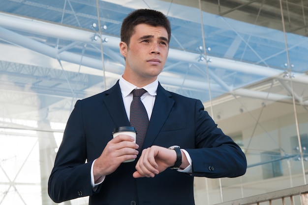 Free photo pensive business man checking time on watch outdoors