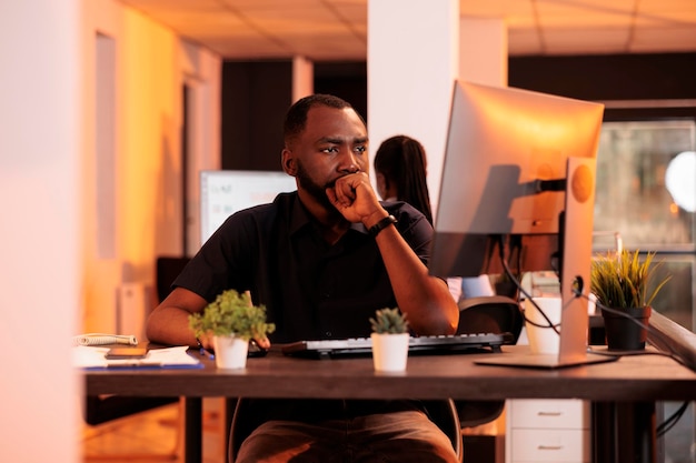 Pensive businessman brainstorming ideas to work on research data, reading email on computer. Thoughtful freelancer being focused about charts report and paperwork in office with big windows.