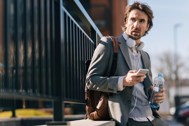 Pensive businessman looking away while text messaging on mobile phone in the city