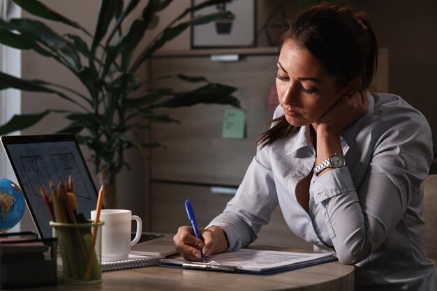 Pensive businesswoman filling out documents while finishing paperwork in the office