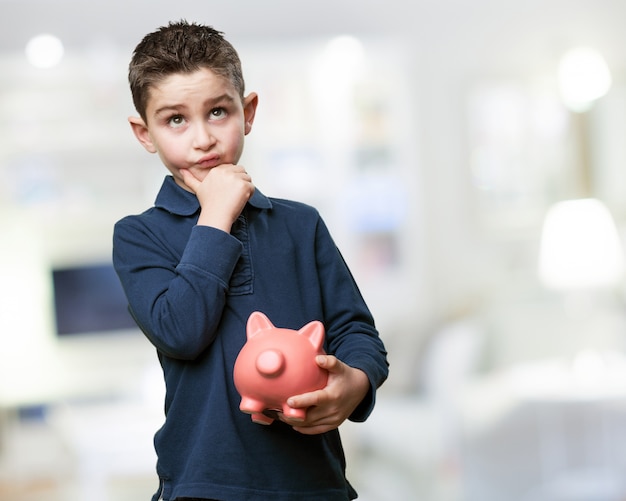 Pensive child with a piggy bank