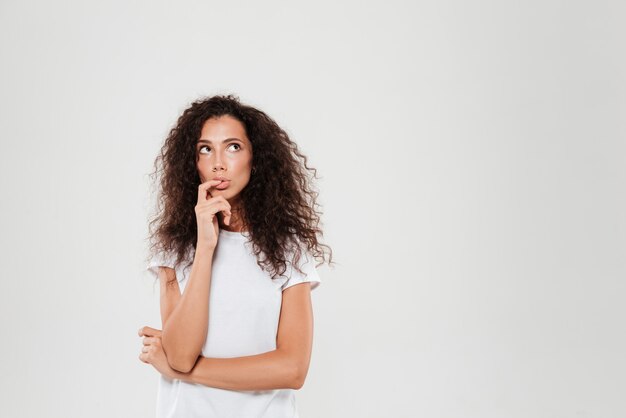 Pensive curly woman with finger near the mouth looking away