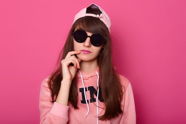 Pensive dark haired teenager, wears pink stylish clothing