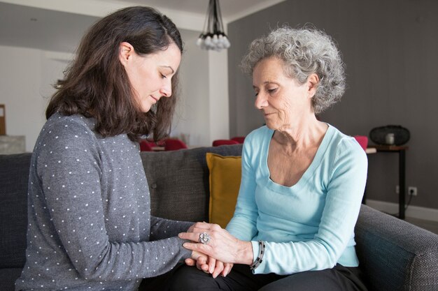 Pensive elderly woman and her daughter holding hands