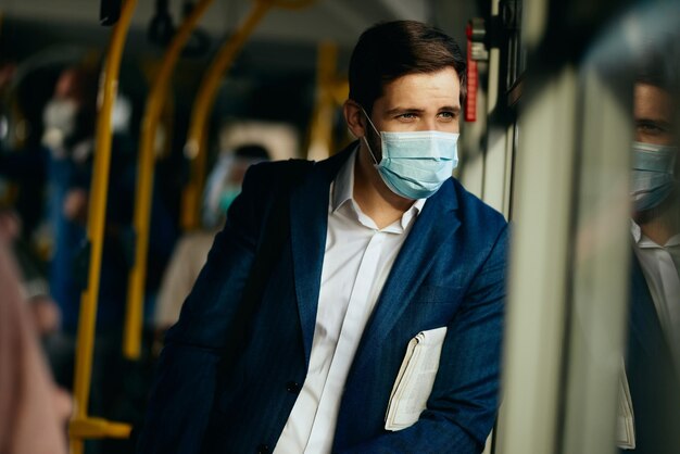バスで通勤中に窓越しに見ているフェイスマスクと物思いにふける起業家