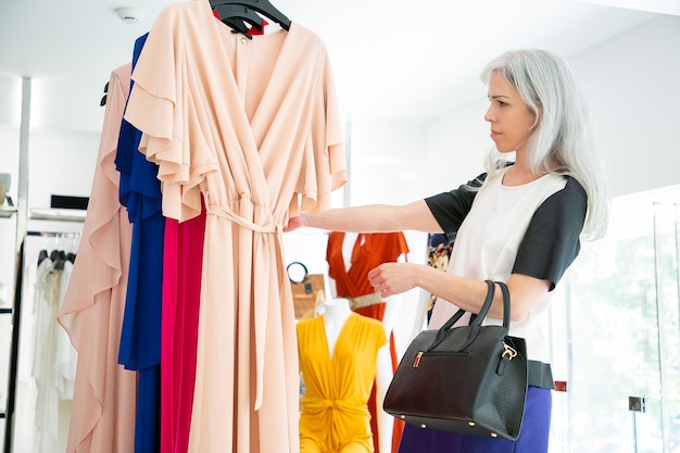 잠겨있는 패션 매장 고객이 옷을 선택하고 랙에서 드레스를 검색합니다. 중간 샷, 측면보기. 패션 스토어 또는 소매 개념