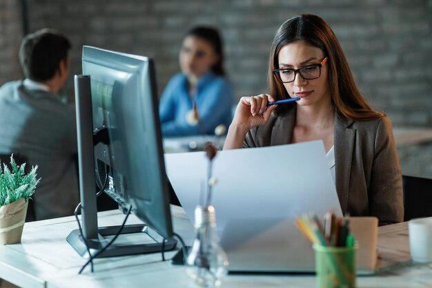 Pensive female architect analyzing blueprints while working in the office