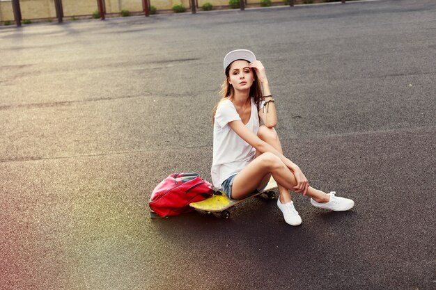 Pensive girl sitting on the skateboard at sunset