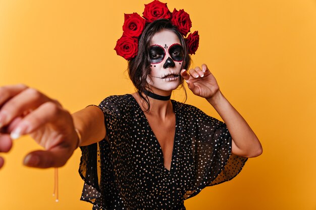 Задумчивая девушка с грустным взглядом карих глаз просит следовать за ней. Портрет темноволосой мексиканской модели на оранжевой стене.