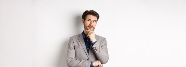 Pensive handsome man in suit looking up and thinking making choice pondering ideas standing against