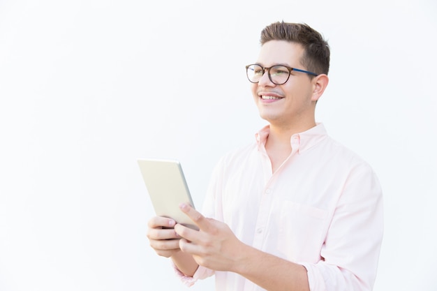 Pensive happy guy in eyeglasses holding tablet