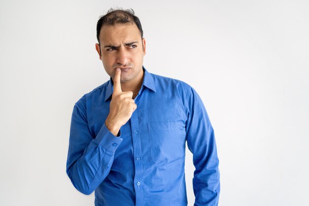 Pensive Indian man touching lips and looking away