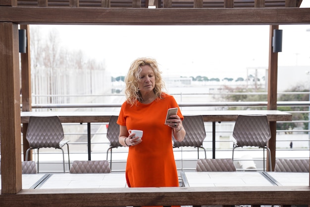 Pensive lady with smartphone drinking coffee