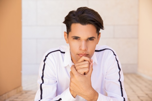 Pensive Latin man touching chin and sitting outdoors