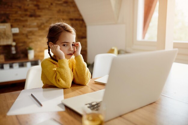 Pensive little girl using laptop at home