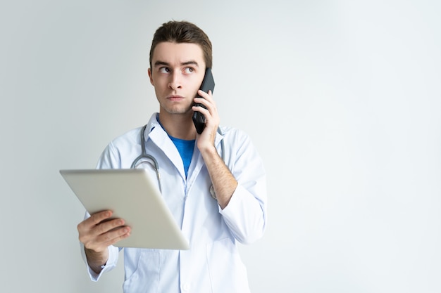 タブレットコンピュータとスマートフォンを使用している夢中の男性医者