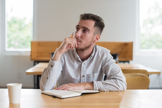 Studente maschio pensieroso che si siede allo scrittorio in aula