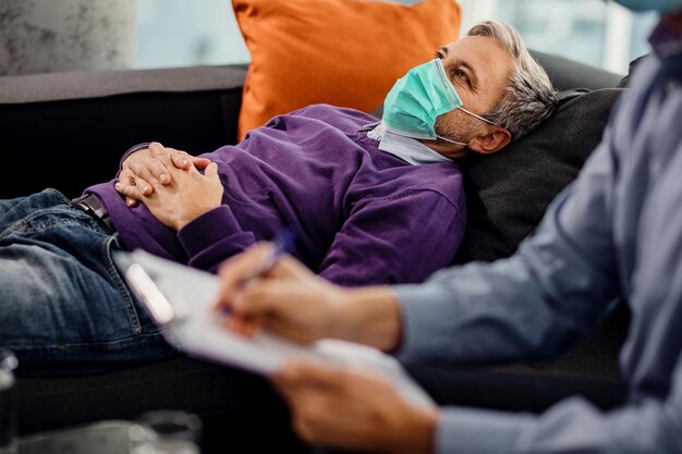 Pensive man wearing protective face mask while having counseling with his psychiatrist