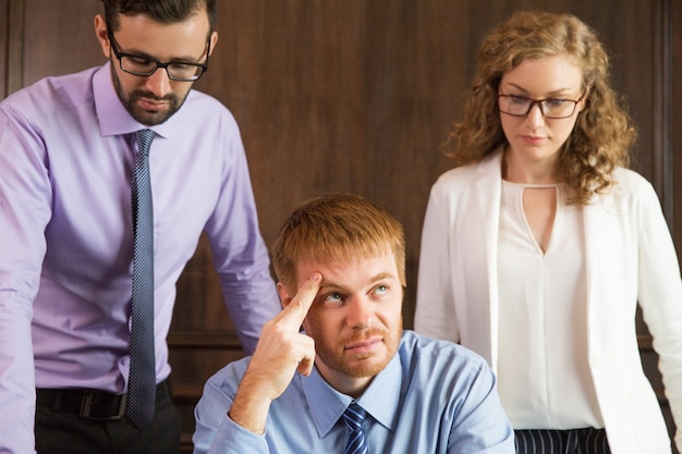 Free photo pensive man with fingers on forehead while his two companions watch him