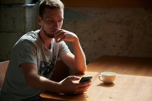 Pensive man working in phone with cup coffee