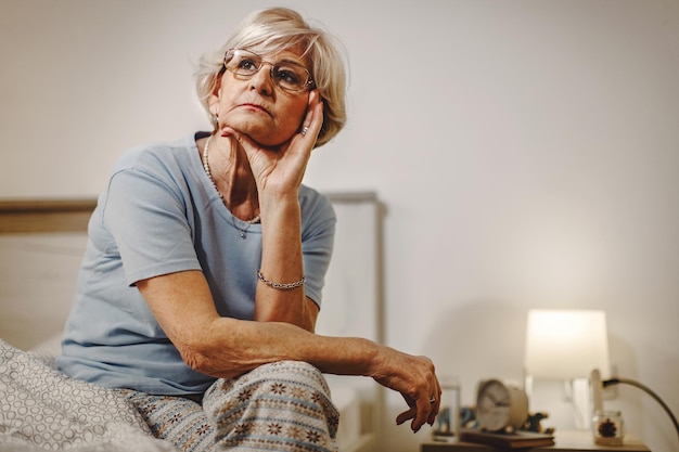 Pensive mature woman thinking of something while sitting on the bed