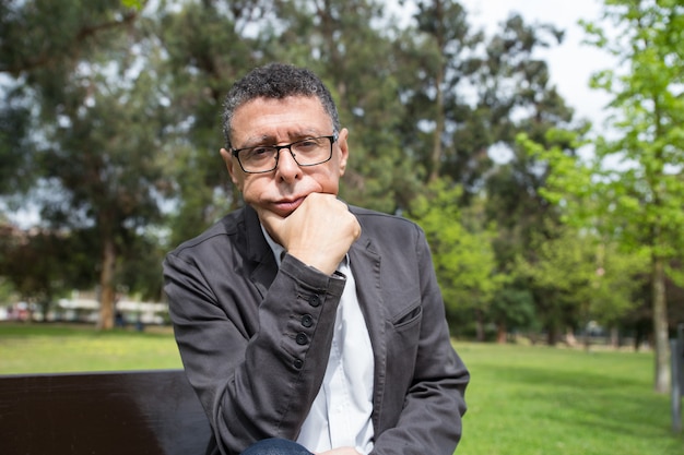 Free photo pensive middle-aged man sitting on bench in city park