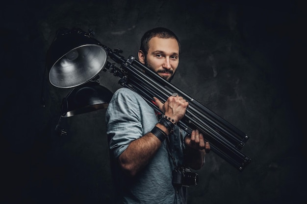 Free photo pensive photographer is holding special lamp for photo set at dark photo studio.