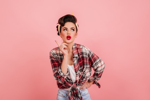 Free photo pensive pinup girl posing on pink background. studio shot of charming brunette woman wearing checkered shirt.